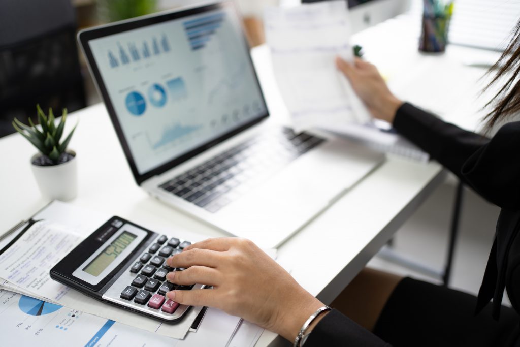 Hand of an Asian female employee is calculating numbers in the office. She was using a calculator on a white table.